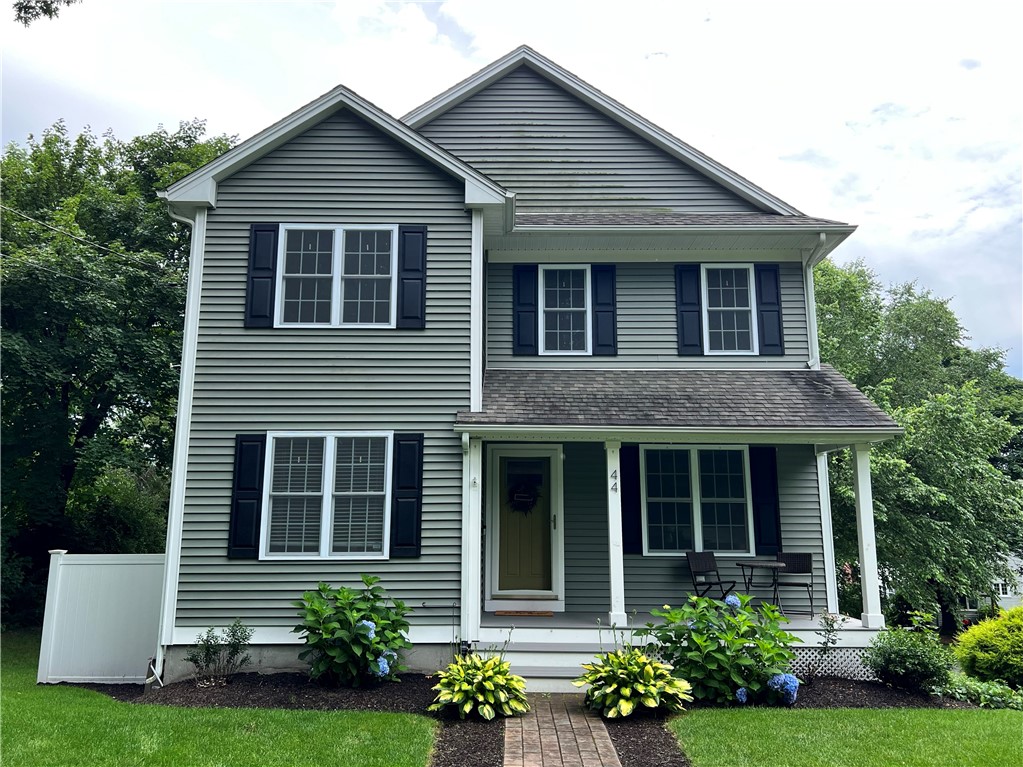 Two-story gray house with dark shutters, a covered porch, and a walkway through landscaped flower beds.