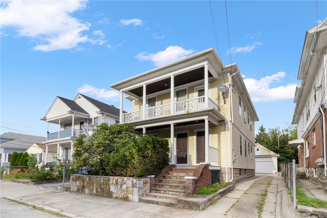 Yellow two-story house with covered porches, brick steps, and a driveway leading to a detached garage.