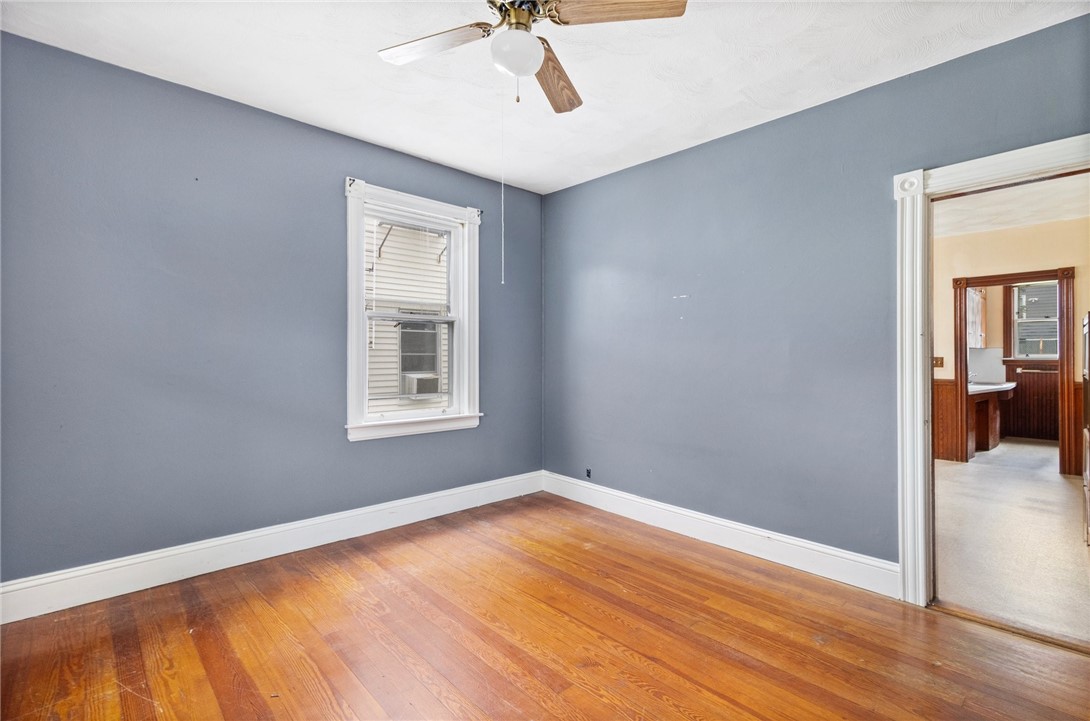 Empty bedroom with blue-gray walls, hardwood floors, ceiling fan, and an adjoining bathroom doorway.