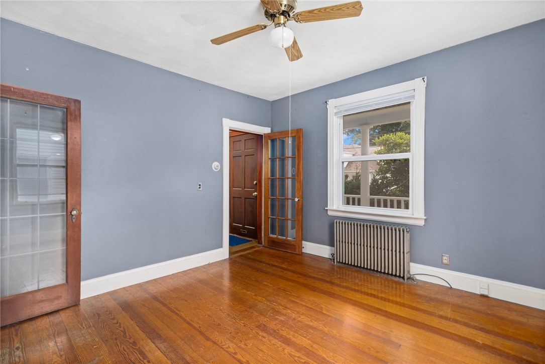 Unfurnished room with blue-gray walls, polished hardwood floors, a window, radiator, and ceiling fan.