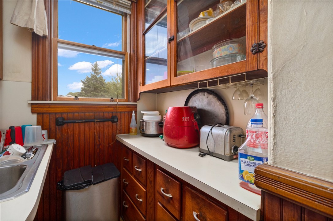 Narrow kitchen with dark wood cabinetry, white counters, and a large window overlooking trees.