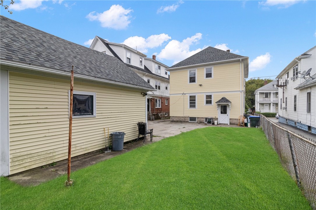 Backyard with a broad green lawn between a yellow house and detached building.