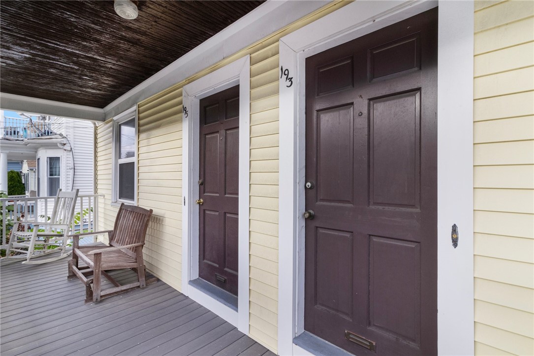 Covered porch with two dark entry doors, pale yellow siding, and wooden rocking chairs.