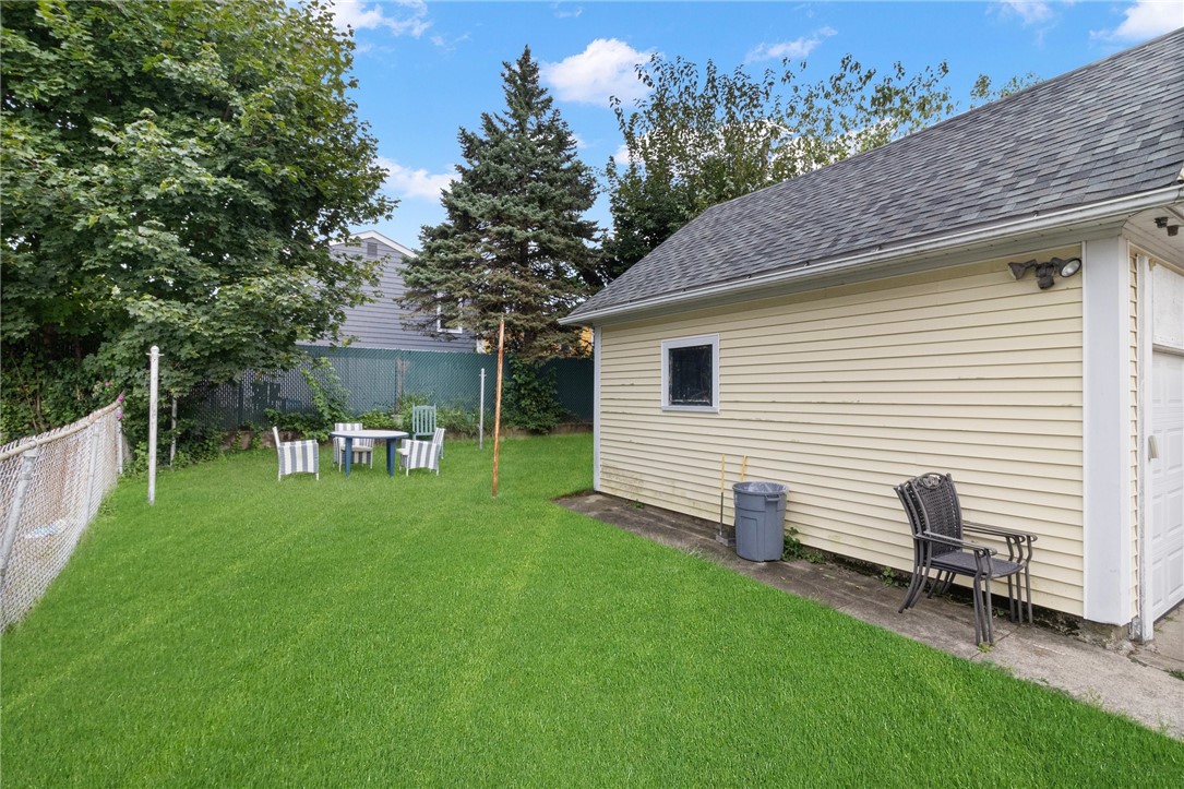 Fenced backyard with a green lawn, outdoor dining set, and detached garage.