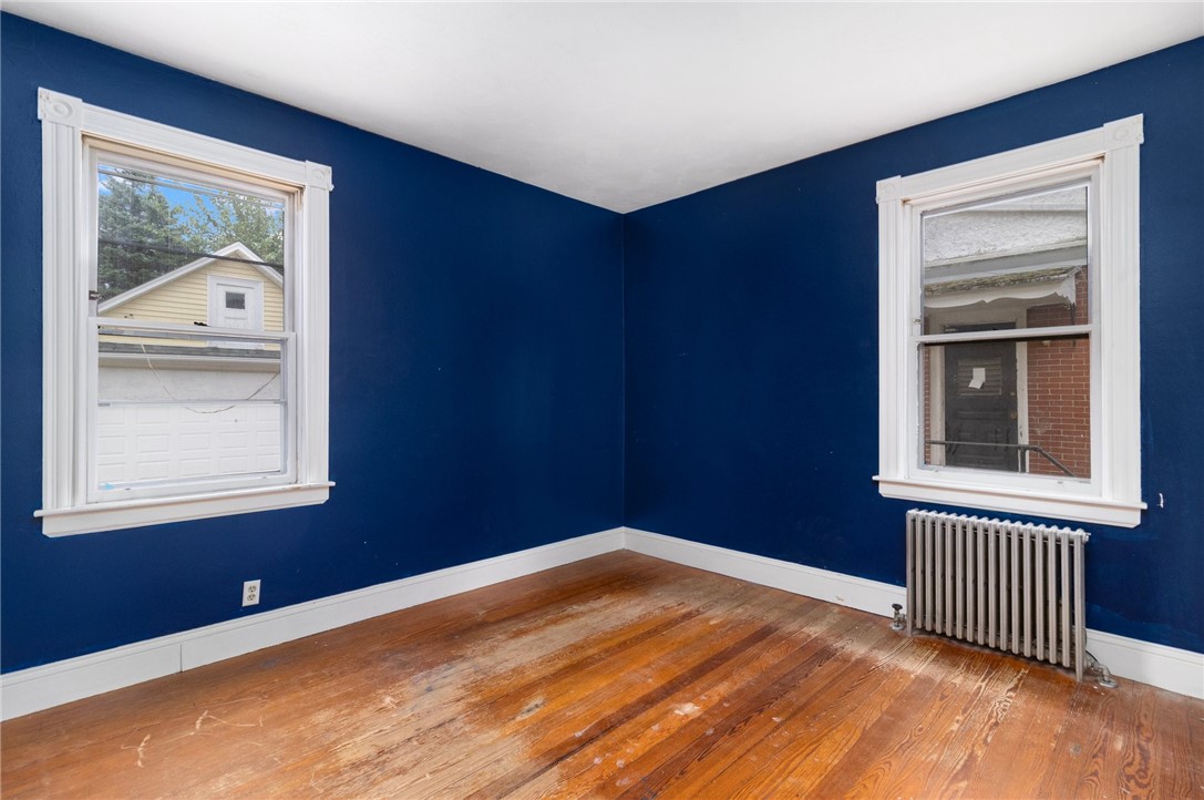 Vacant blue room with two windows, a radiator, and worn hardwood floors.