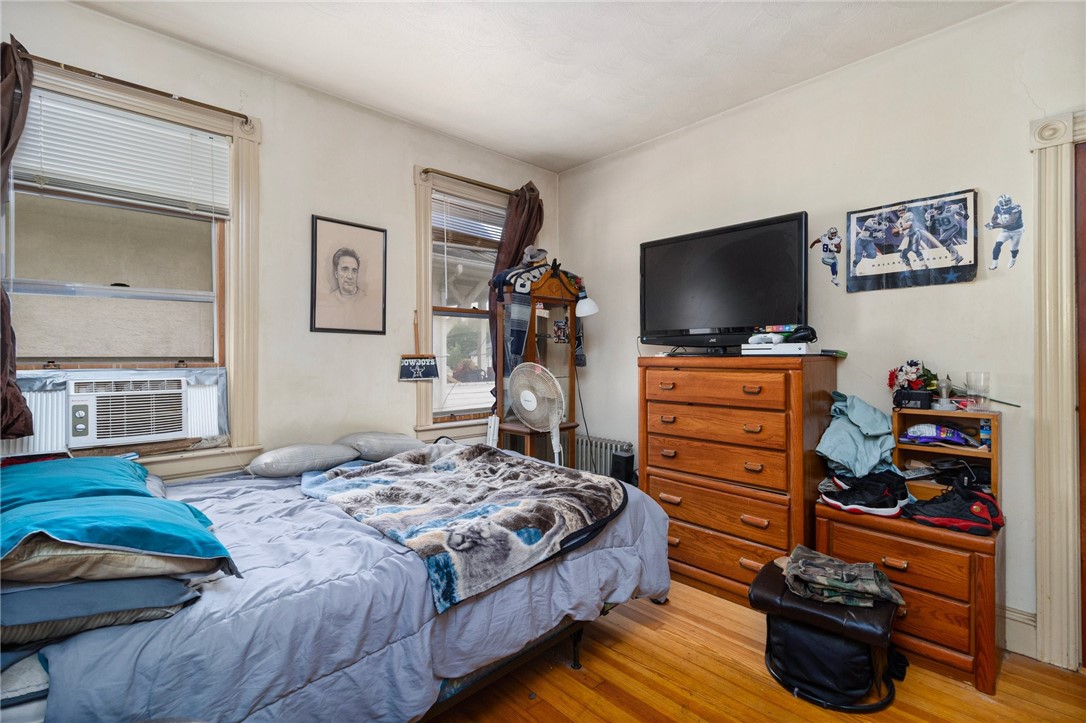 Bedroom with blue-gray bedding, a wooden dresser and television, sports decorations, and hardwood floors.