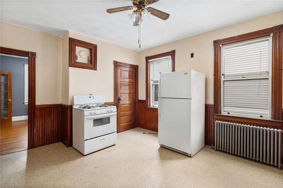 Kitchen with dark wood wainscoting, white appliances, and a radiator beneath the window.