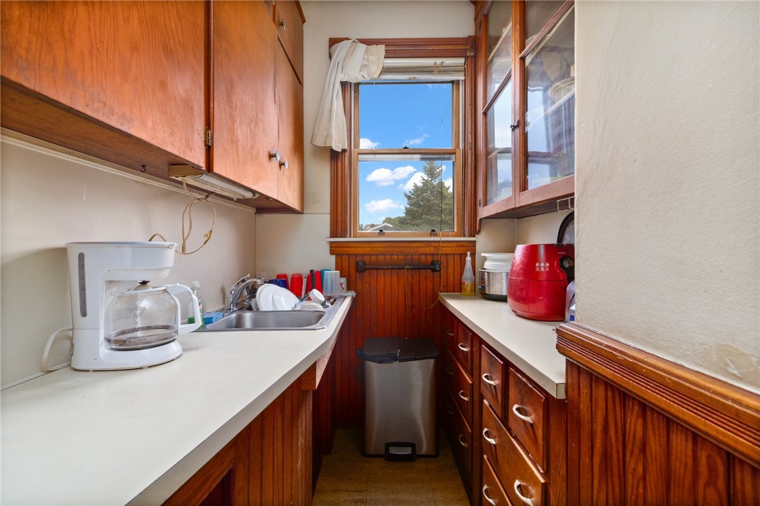 Narrow galley kitchen with warm wood cabinetry, white counters, and a window overlooking trees.
