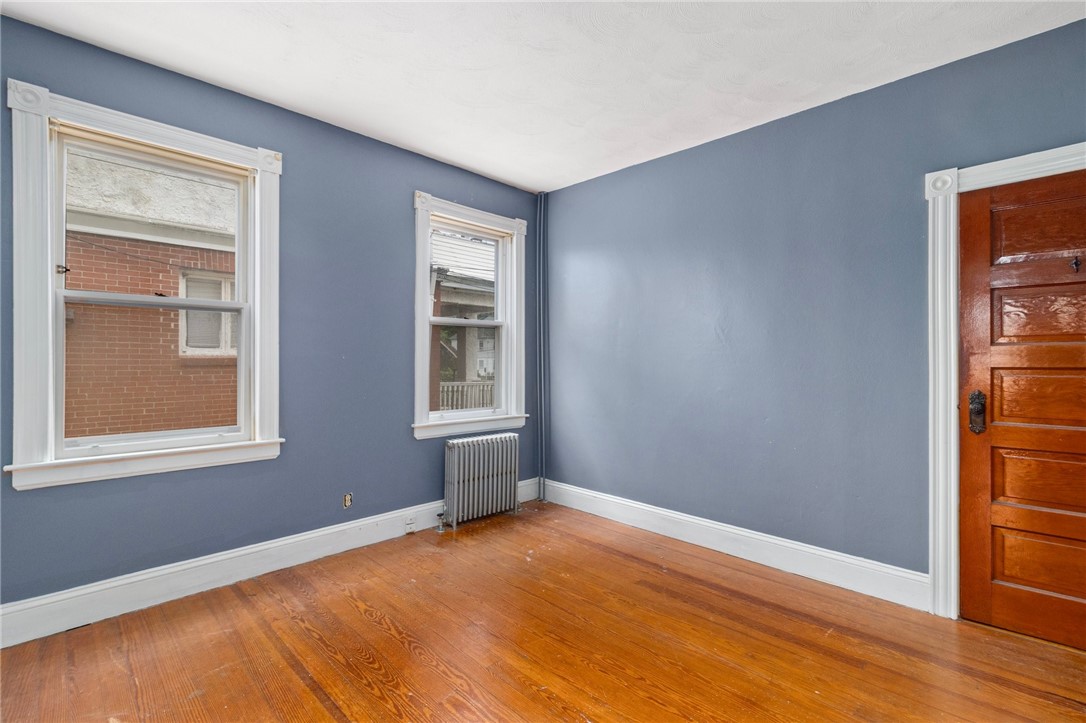 Vacant room with blue walls, two windows, a radiator, and polished hardwood floors.
