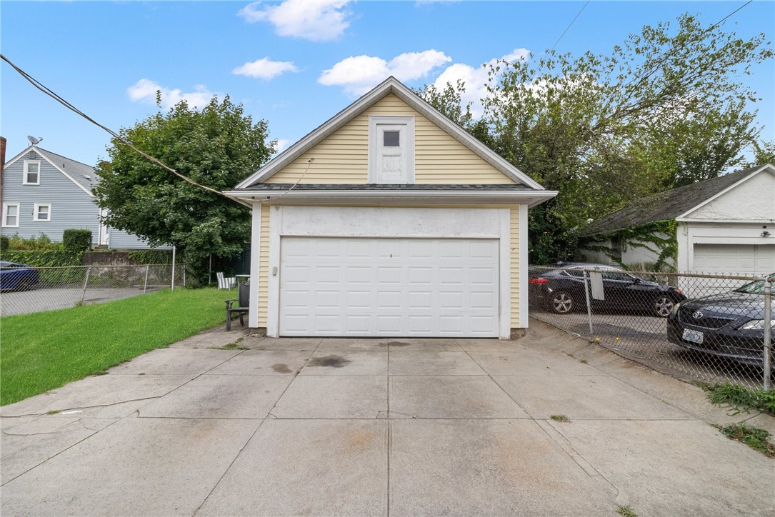 Detached beige garage with a white double door, viewed from its concrete driveway.