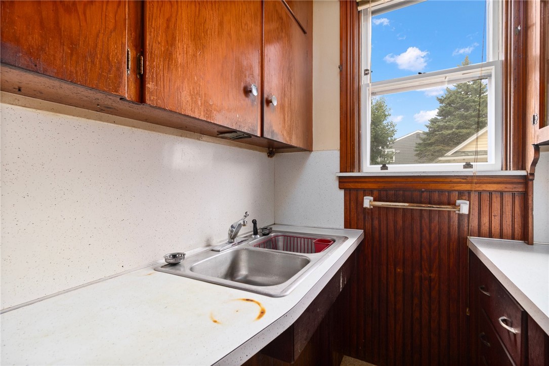 Kitchen with reddish wood cabinetry, speckled countertops, and a double sink beneath a window.