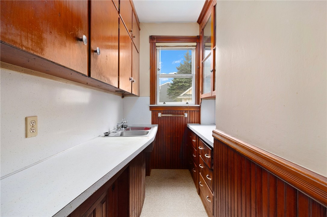 Galley kitchen with dark wood cabinetry, white countertops, and a window at the far end.