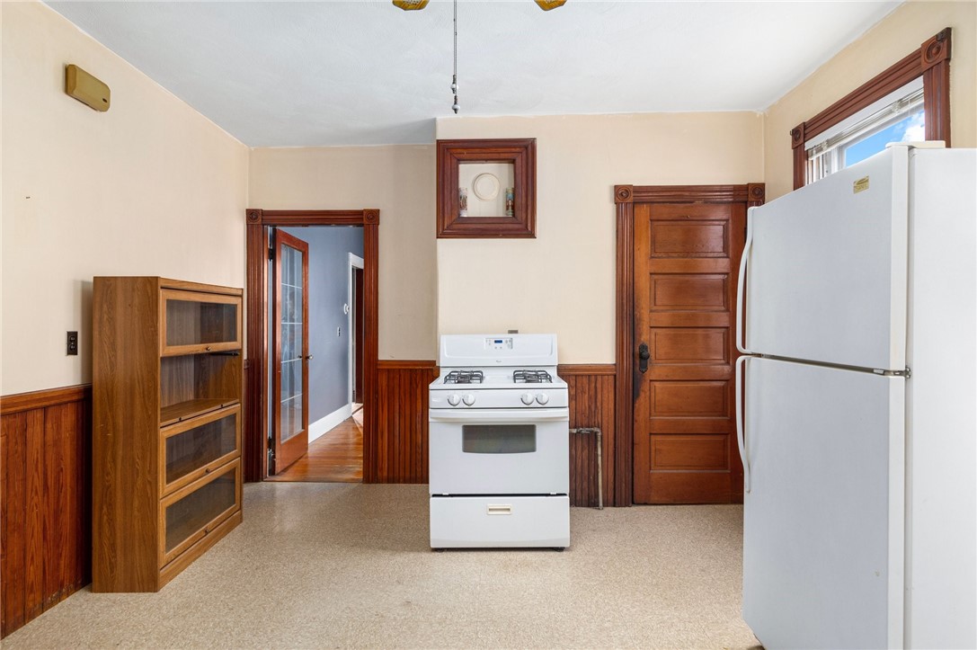 Kitchen with white stove and refrigerator, wood-paneled walls, and dark wood trim.