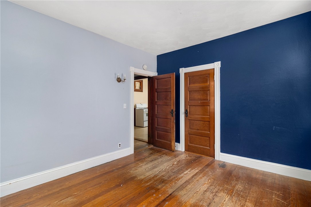 Empty room with hardwood floors, a deep blue wall, and wooden doors opening toward a kitchen.
