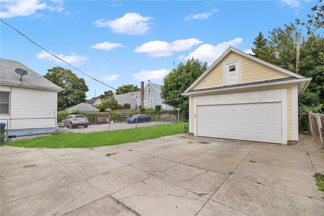 Detached yellow garage with a white double door and a wide cracked concrete driveway.