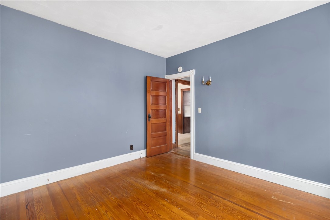 Empty room with blue-gray walls, polished hardwood floors, and an open wooden door.