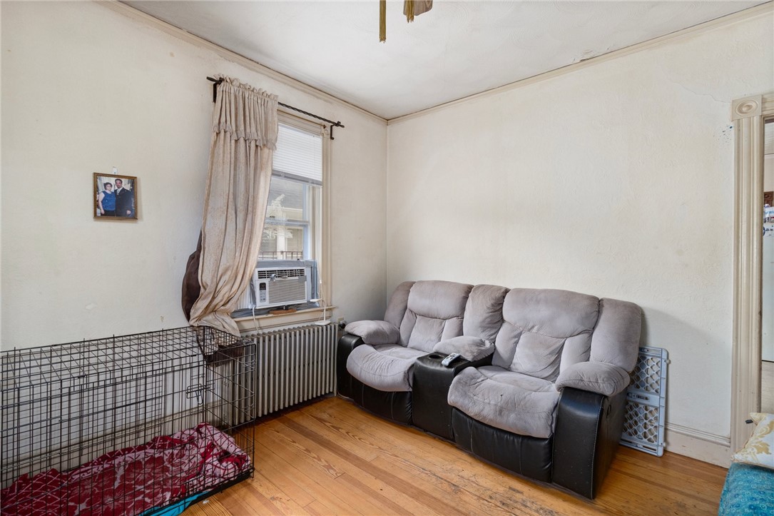 Living room with a gray reclining loveseat, hardwood floors, window air conditioner, and dog crate.