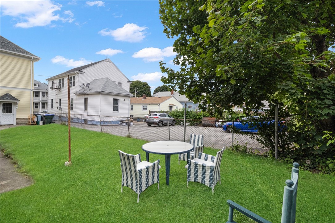 Backyard with a round patio table and woven chairs on a lawn beside a chain-link fence.