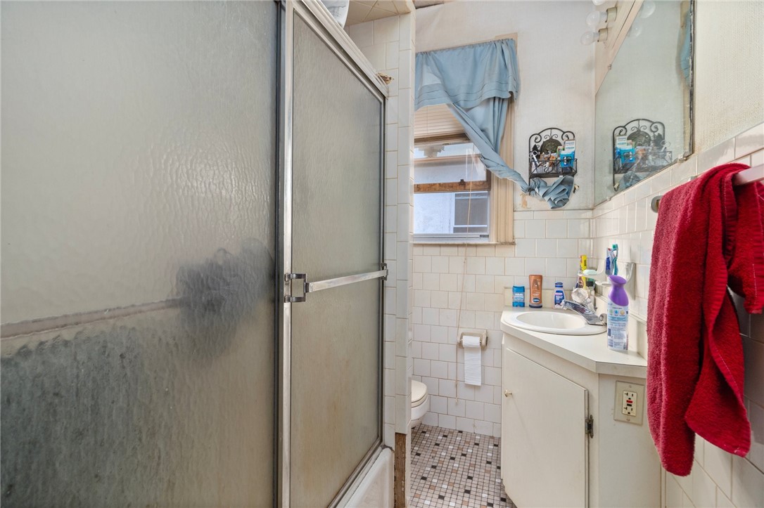 Bathroom with a frosted-glass shower, tiled walls, and a small vanity beneath a mirror.