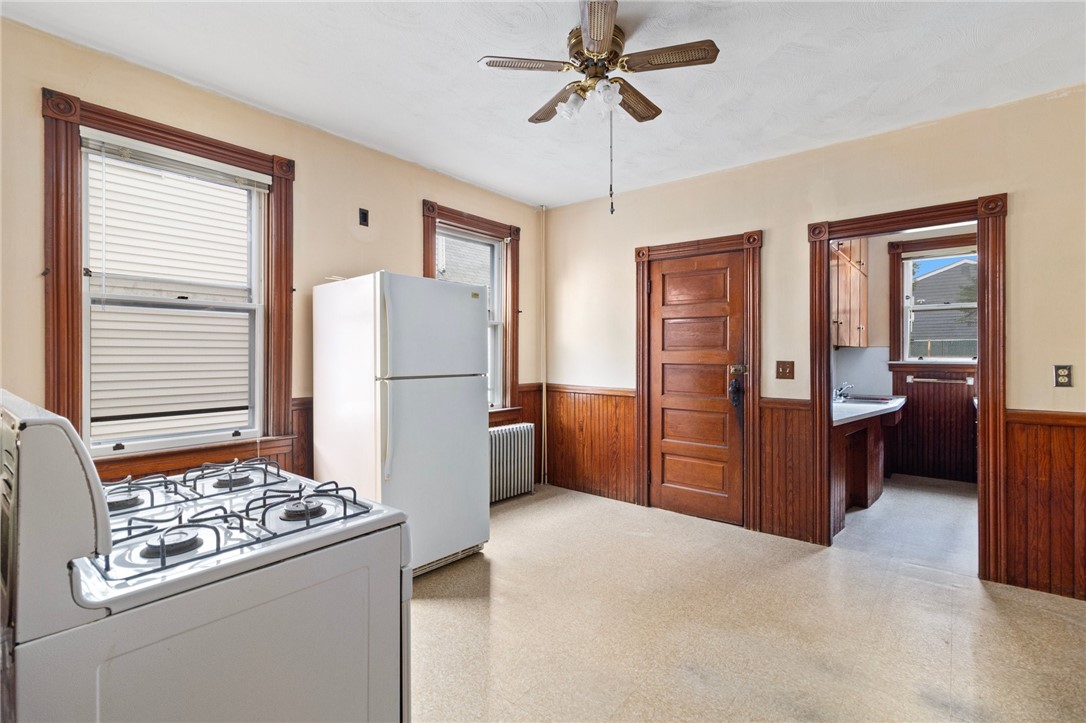 Kitchen with a gas range, refrigerator, dark wood wainscoting, and doorway to an adjoining room.