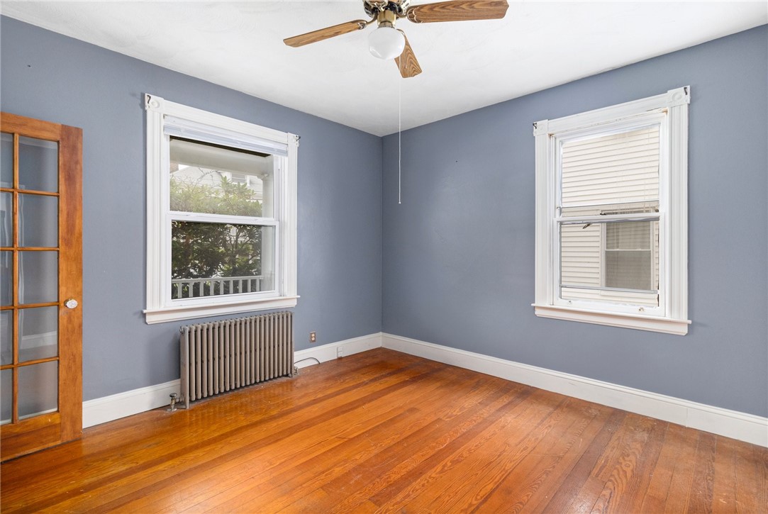 Empty room with blue-gray walls, hardwood floors, two windows, and a radiator.