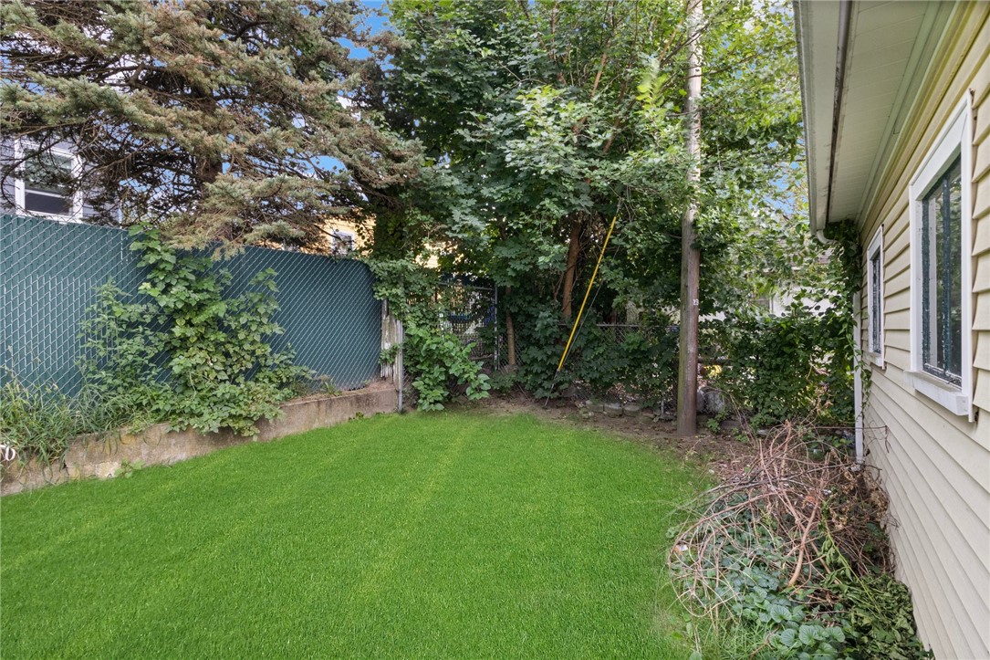 Shaded backyard with a green lawn, chain-link fence, and mature trees beside the house.