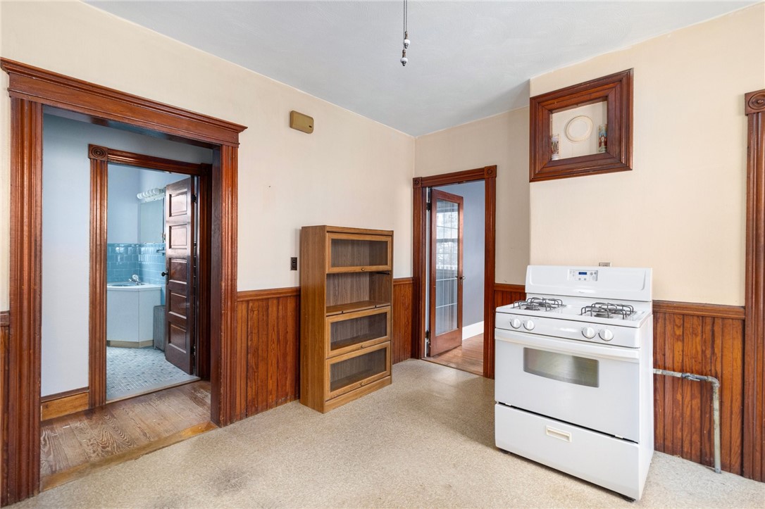 Room with a white gas stove, dark wood wainscoting, and a doorway to a tiled bathroom.