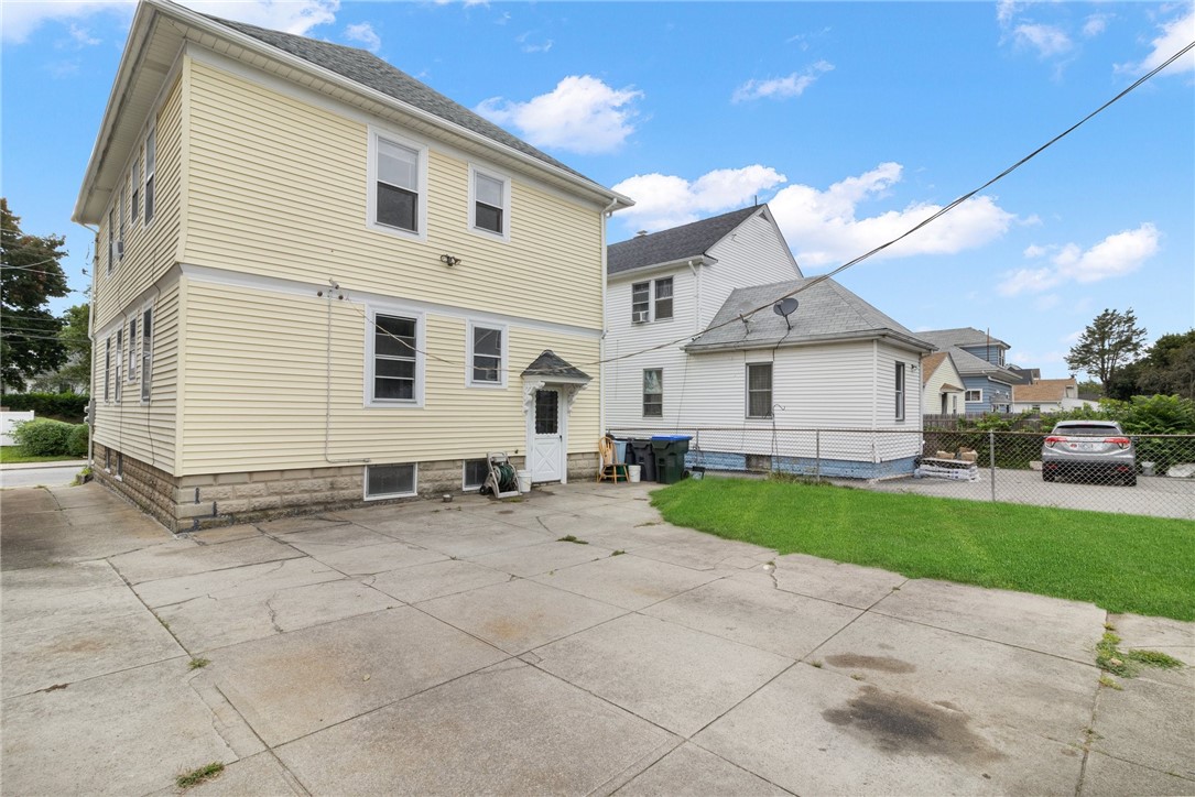 Pale yellow two-story house with a side entrance, paved driveway, and small lawn.