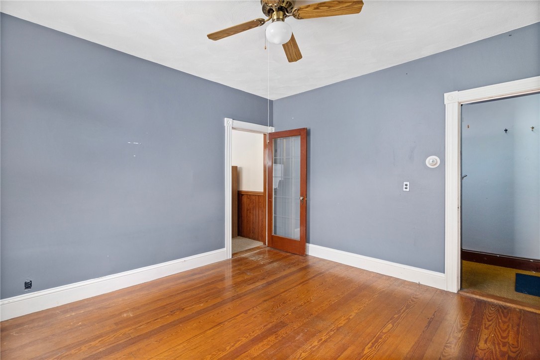 Empty room with blue-gray walls, hardwood floors, a ceiling fan, and a glass-panel door.