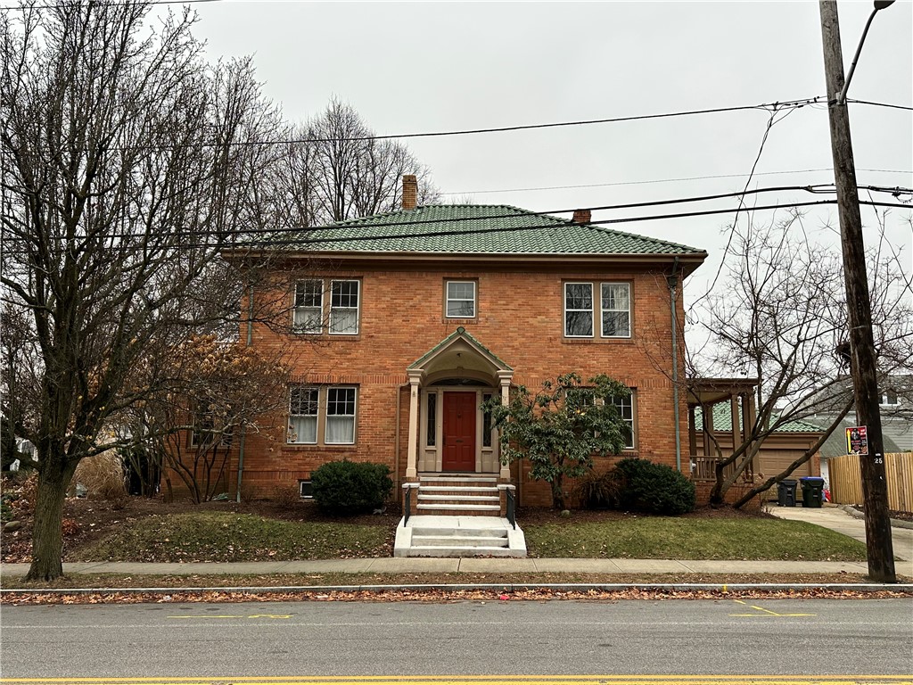 Two-story red brick house with a green tiled roof and a red front door beneath a peaked entry.