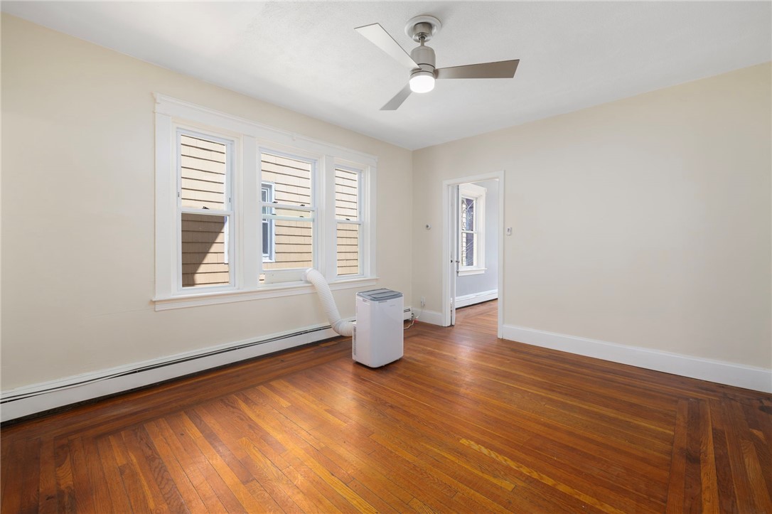 Empty room with polished hardwood floors, three windows, and a portable air conditioner.