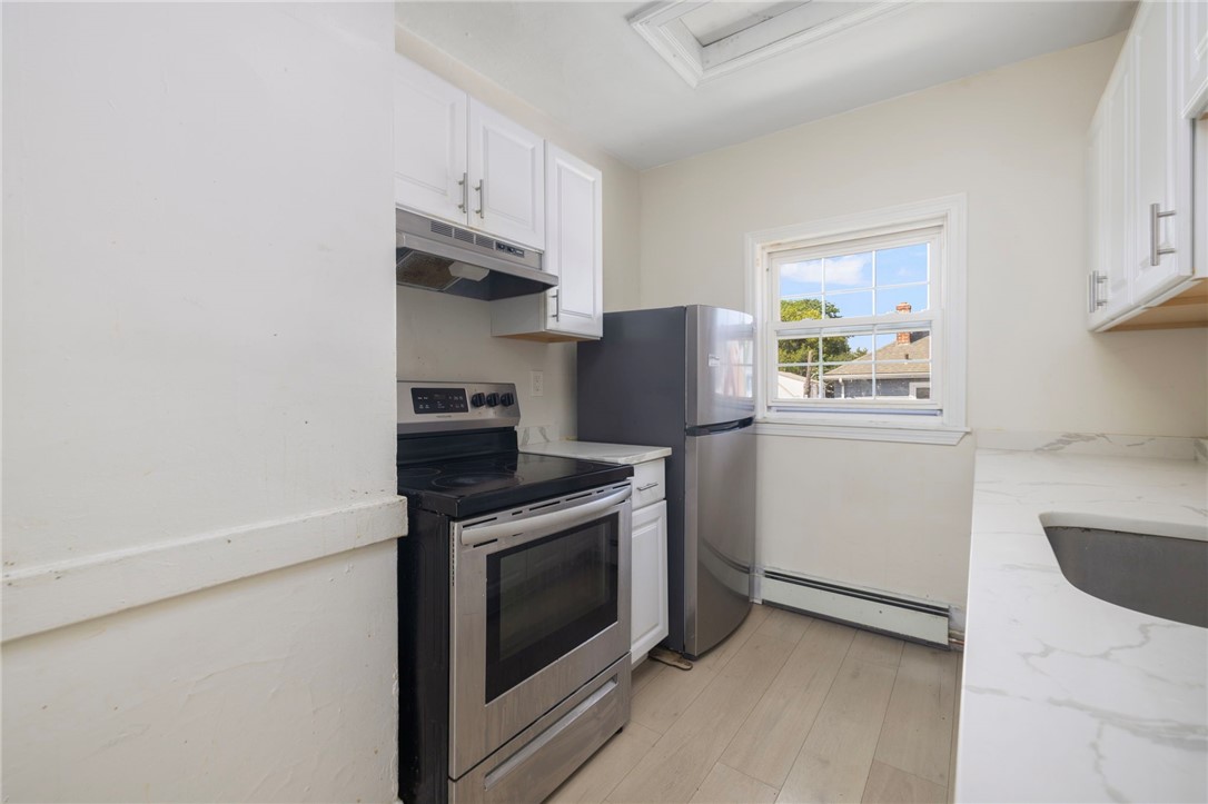 Kitchen with white cabinets, stainless steel appliances, and a window overlooking neighboring rooftops.