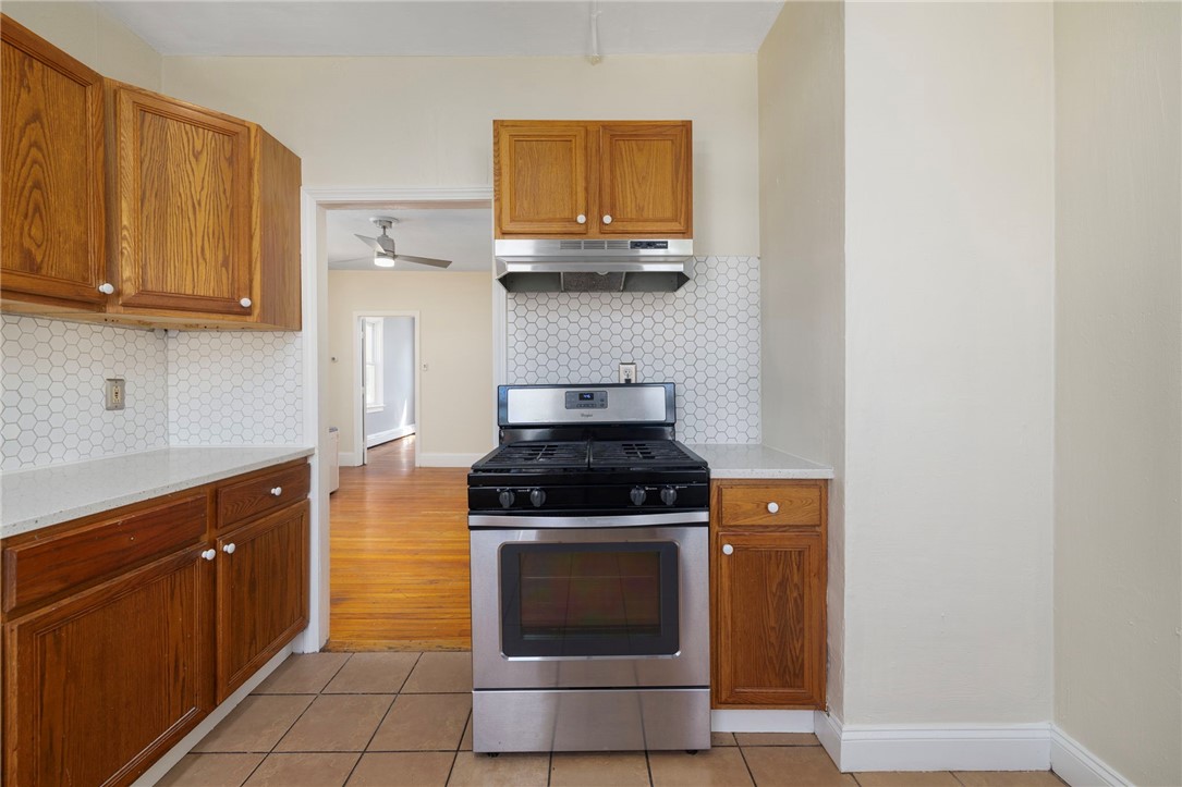 Kitchen with wood cabinets, hexagonal tile backsplash, and stainless-steel range.