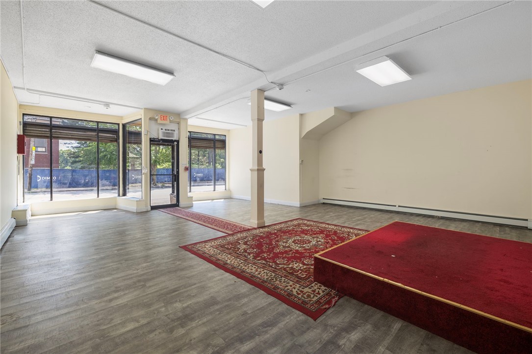 Vacant storefront interior with broad front windows and a red-carpeted raised platform.