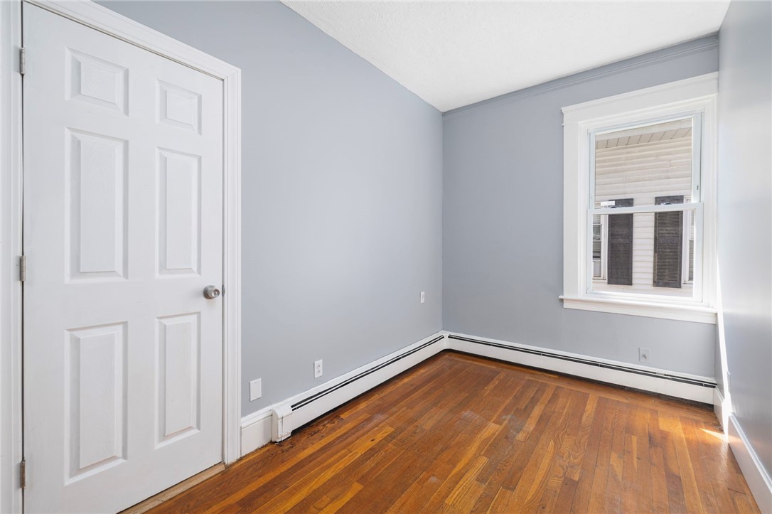 Empty room with polished hardwood floors, gray walls, and a white-trimmed window.