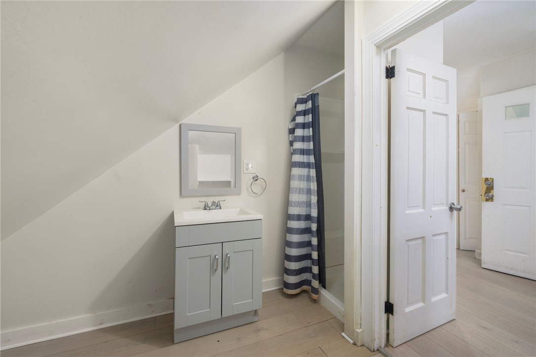 Bathroom with a white vanity beneath a sloped ceiling and a blue-striped shower curtain.