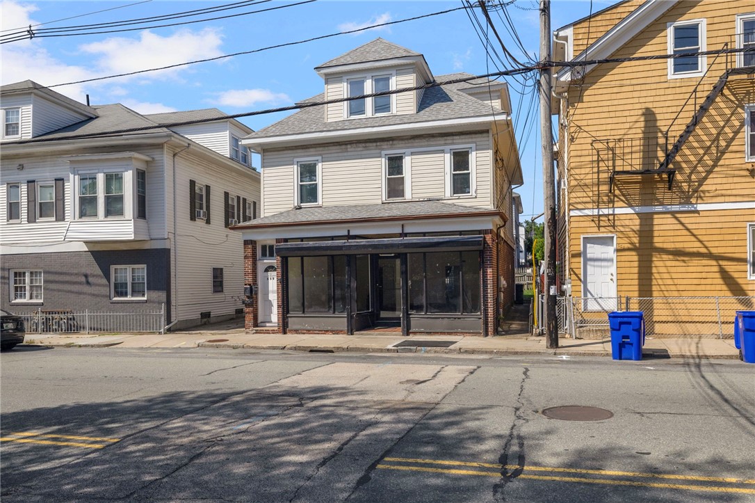 Two-story street-facing building with a dark-framed enclosed storefront and overhead utility wires.
