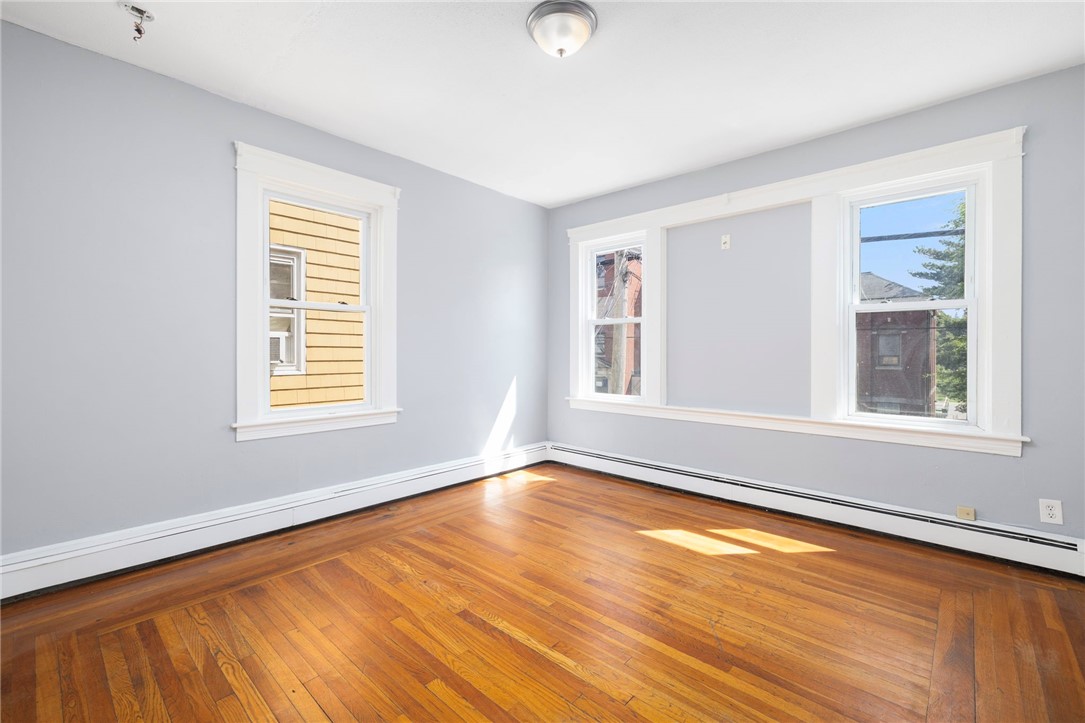 Vacant room with polished hardwood floors, gray walls, and three windows.