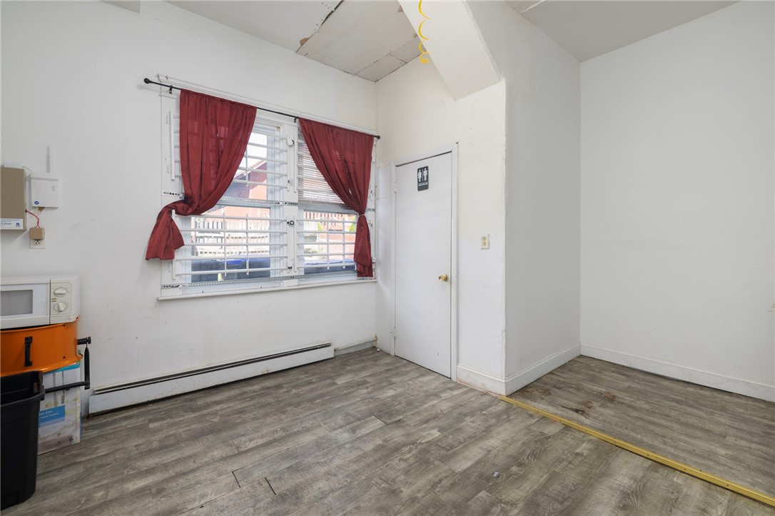 Empty room with gray wood-look flooring, red curtains, and a restroom door.