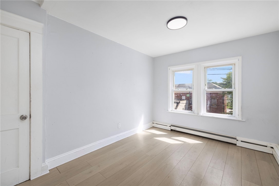 Empty room with pale wood flooring, two windows, and baseboard heating.