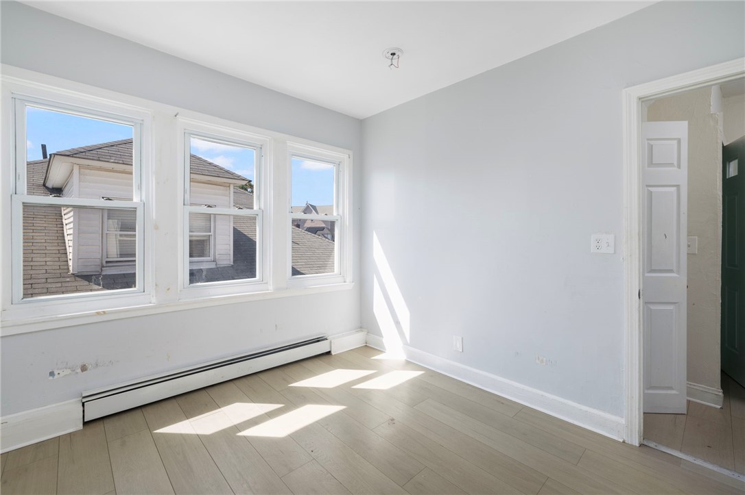 Empty room with three windows, pale wood-look flooring, and a baseboard heater.