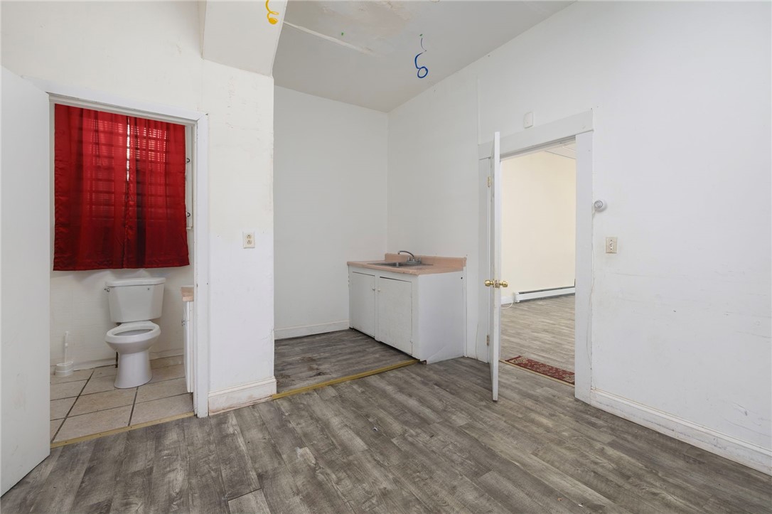 Vacant room with gray plank flooring, a small sink cabinet, and an adjoining bathroom with red curtains.