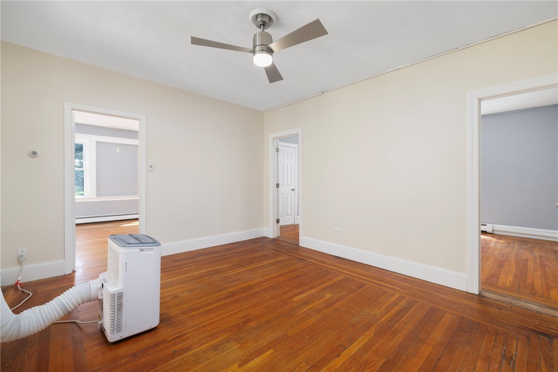 Unfurnished room with polished hardwood floors, a ceiling fan, and doorways to adjoining rooms.