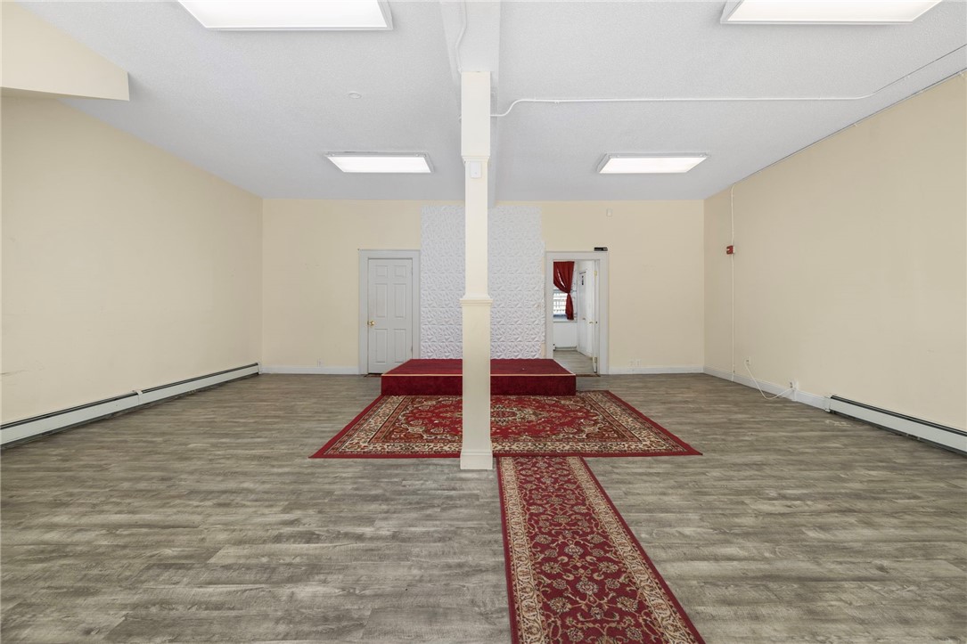 Vacant interior room with a central support column, gray flooring, and red rugs leading to a raised platform.