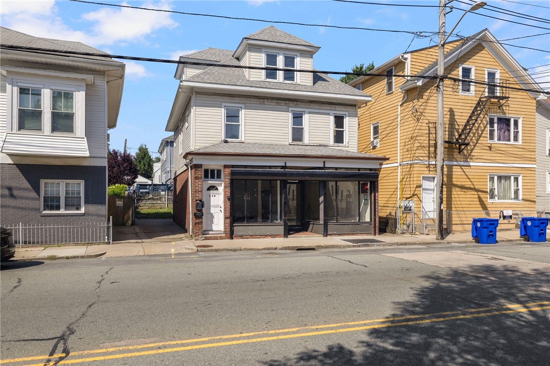 Two-story commercial building with a glass storefront and brick ground floor on a residential street.
