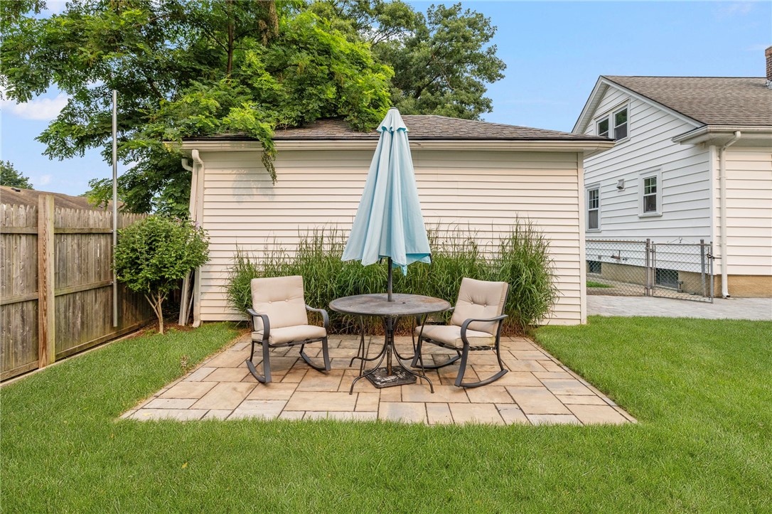 Backyard patio with two chairs and a table beneath a closed umbrella.