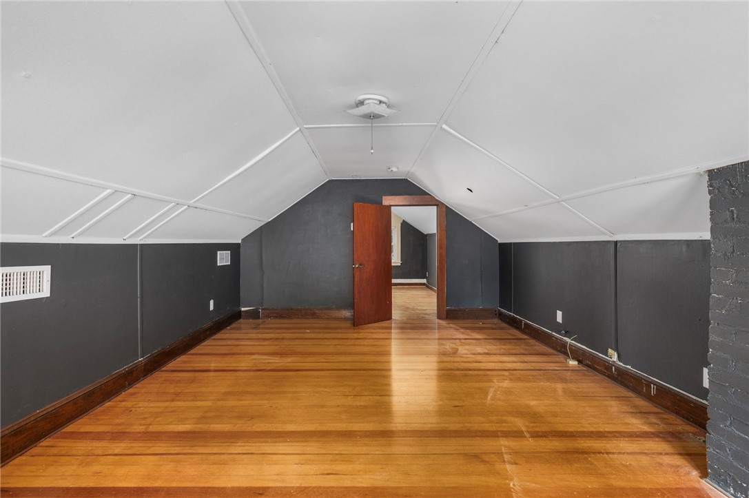 Vacant attic room with sloped ceiling, charcoal walls, and polished hardwood floors.