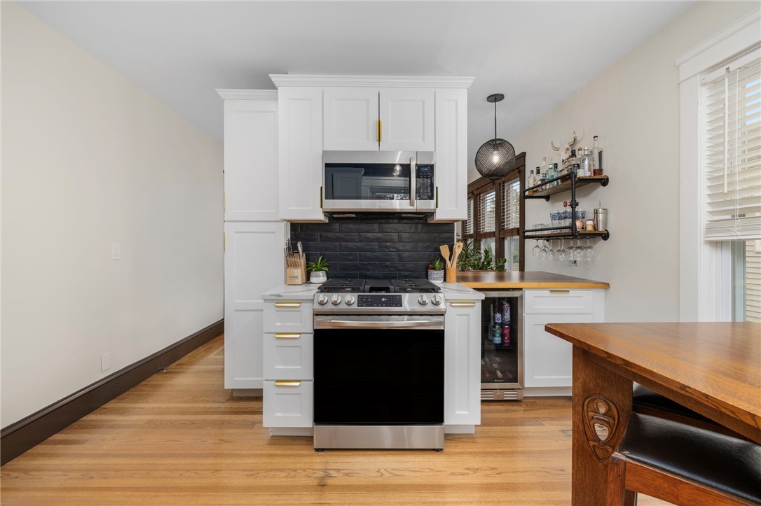 Kitchen with white cabinetry, stainless steel appliances, a black tile backsplash, and warm wood floors.