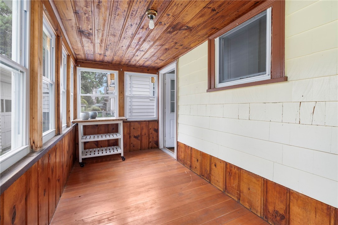 Enclosed porch with a wood ceiling and flooring, tall windows, and a small rolling shelf.