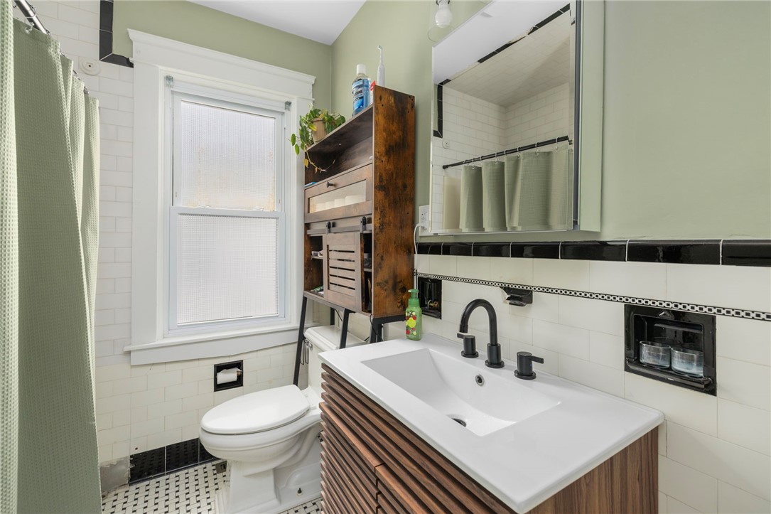 Bathroom with a wood-slat vanity, white sink, tiled shower, and frosted window.
